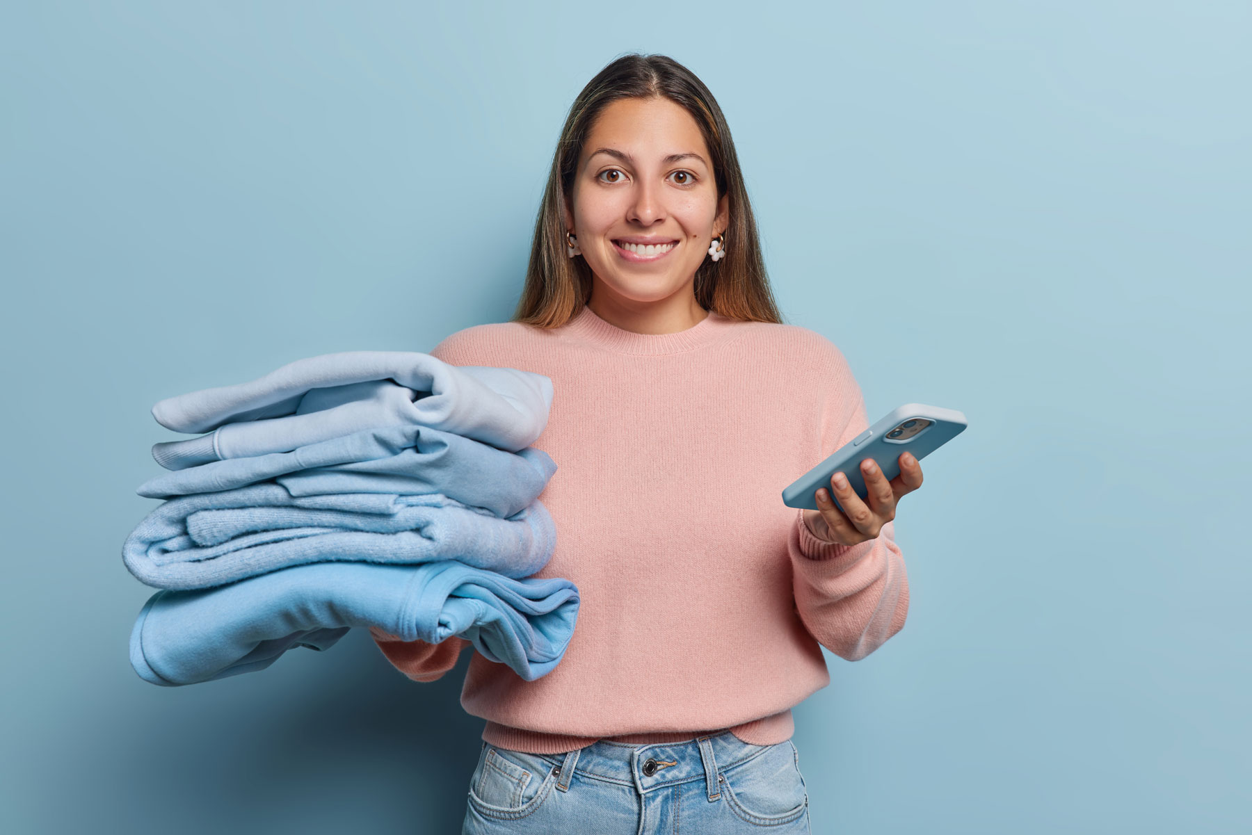 Person holding a stack of freshly folded laundry and a smartphone